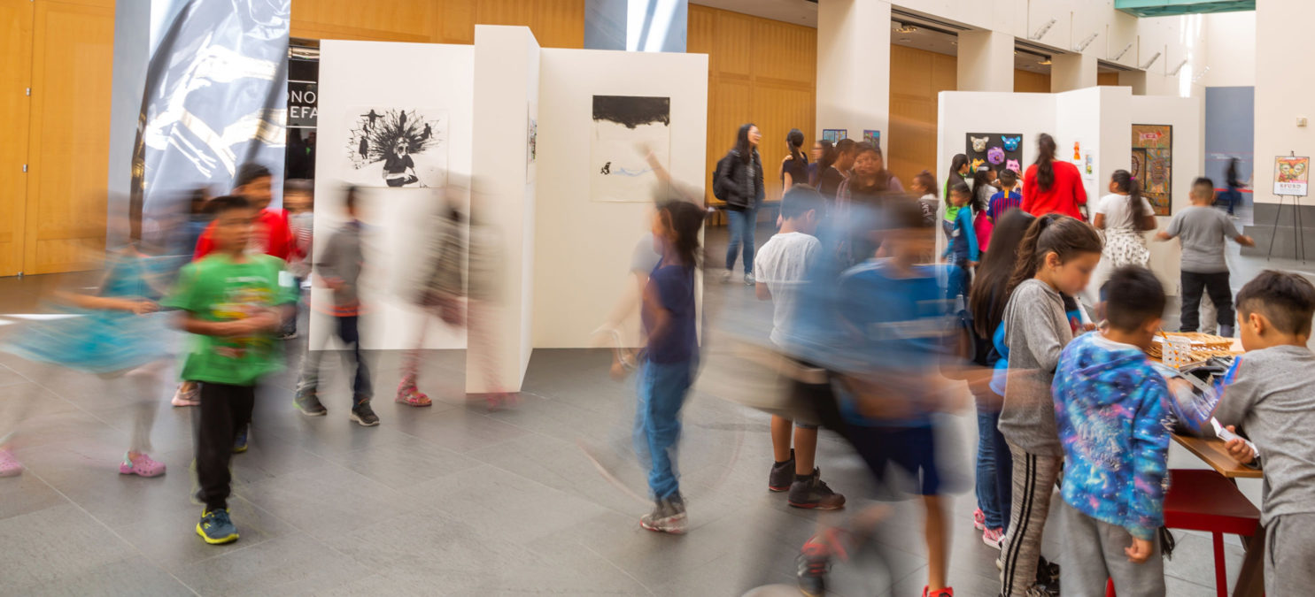 Elementary aged students moving around gallery walls with mounted art