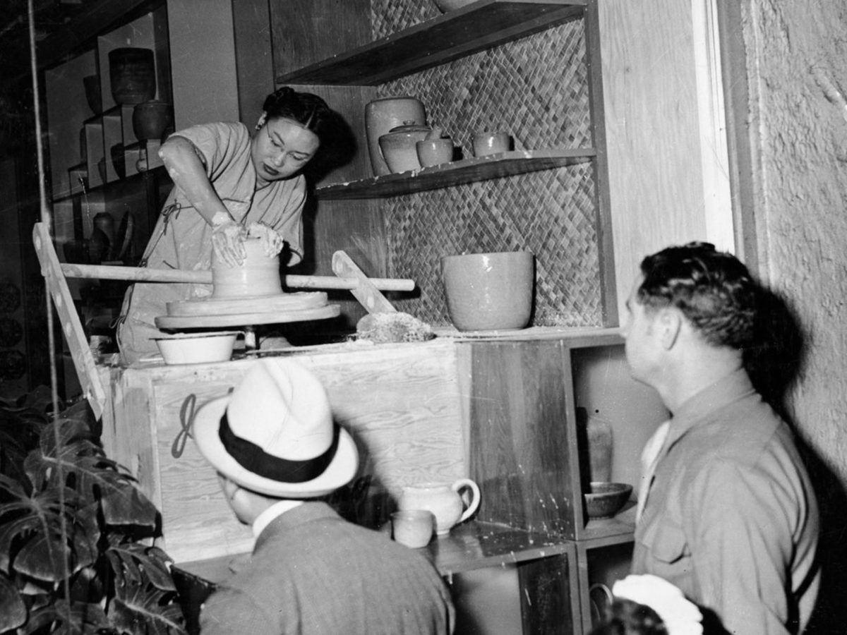 A woman sculpts clay while two men look on.